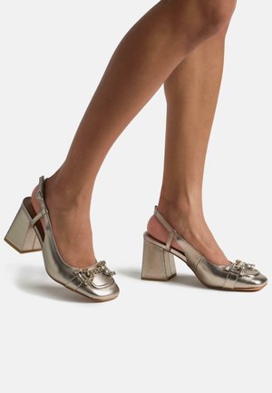 Metallic gold slingback heels with a rounded toe, chunky block heel, and decorative bow detail adorned with small beads.