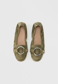 Mocasines de ante en verde oliva. Forma redondeada con un detalle de hebilla circular plateada y costuras en contraste. Acabado suave y texturizado.