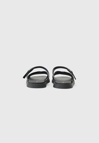 Black sandals with two wide straps and a braided design. Flat sole with minimalistic style and silver buckle detail.