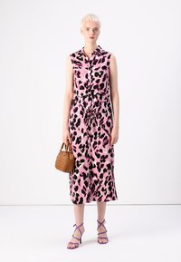 Ροζ αμάνικο φόρεμα με μαύρη και φούξια λεοπάρ εκτύπωση, δεμένο στη μέση. Το μοντέλο κρατά μια πλεκτή καφέ τσάντα, φορώντας μωβ σανδάλια με λουράκια.