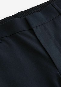 Gros plan sur la taille d'un pantalon bleu marine foncé avec dos élastique et devant plat, montrant la texture du tissu et les détails des coutures.