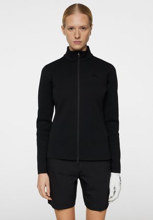 Svart zip-up tröja med hög krage, figurformad design och texturerat tyg. Bärs med svarta shorts och en vit handske på höger hand.