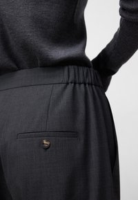 Donkergrijze broek van een gestructureerde stof, met een relaxte elastische tailleband en een achterzak met een knoopsluiting.