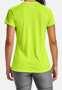 Ljus limegrön idrottströja med korta ärmar, slät textur, subtil logotyp vid halsringningen, bärs med grå figurnära leggings.