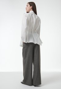 Blusa blanca estructurada con hombros con volantes y un dobladillo tipo peplum, acompañada de pantalones grises de pierna ancha con una tela texturizada.