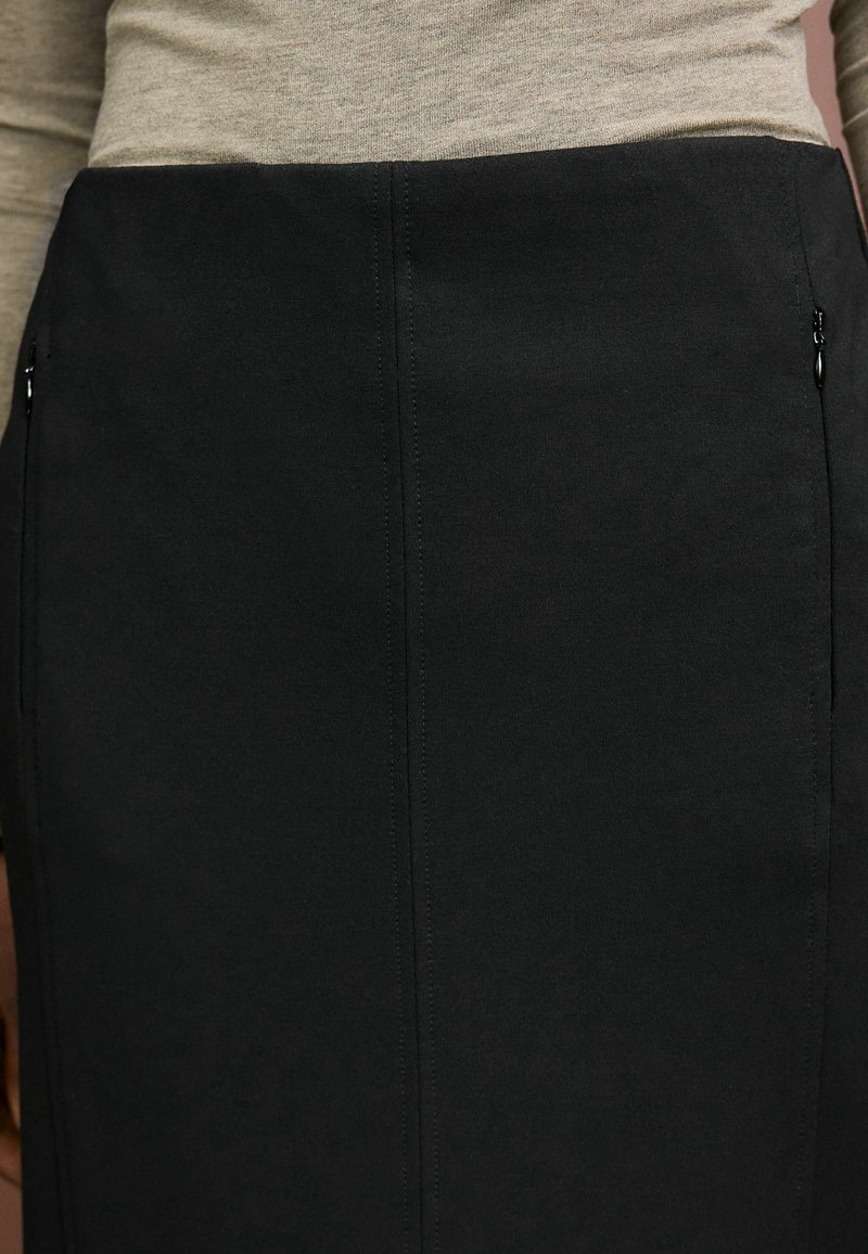 Jupe crayon noire en tissu texturé, dotée de deux fermetures éclair latérales et de coutures arrière pour une silhouette ajustée.