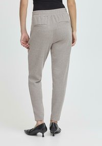 Šedé kalhoty s houndstooth vzorem a elastickým pasem, zúžený střih a dvě zadní kapsy. Nosené s černými vyvýšenými botami.