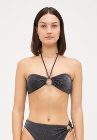 Juoda žvilganti bandeau bikini su sukurtu audiniu, sidabriniu akcentu centre ir derančiais žemais kelnaitėmis su šoninėmis detalėmis.