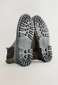 Pruunist nahast pahkluu saapad elastsete külgede ja tekstureeritud mustade kummitaldadega, millel on sügavad mustrid haardumise tagamiseks.