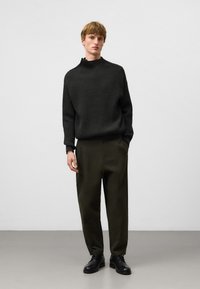 Dikke zwarte geribbelde trui met hoge hals, gecombineerd met olijfgroene op maat gemaakte broek en zwarte veterschoenen. Minimalistisch ontwerp, gladde textuur.