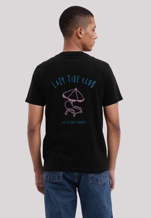 Schwarzes Baumwoll-T-Shirt mit dem Text "Lazy Tide Club" in Blau und Rosa, mit einem Grafikmotiv eines Liegestuhls und einer Sonnenschirm auf der Rückseite.