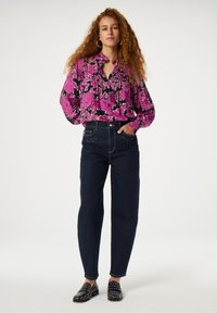 Floral blouse featuring pink flowers on a black background, paired with dark blue high-waisted jeans and black shoes with silver studs.
