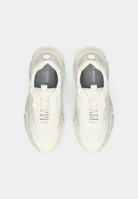 Un par de zapatillas de color crema de Steve Madden con suelas gruesas y detalles de malla, vistas desde arriba sobre un fondo blanco.