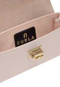 Jasnoróżowe wnętrze skórzanej torby z złotym zapięciem na klamrę. Posiada gładką fakturę oraz czarną metkę marki Furla na satynowej podszewce.