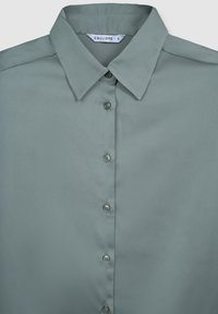 Camicia button-up in morbido tessuto verde chiaro con texture liscia. Presenta un colletto tradizionale e sei bottoni coordinati lungo la parte anteriore.