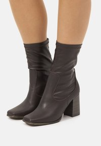 Braune Leder-Ankle-Boots mit lässigem Schaft, quadratischer Spitze und Blockabsatz mit Holztextur. Glatte Oberfläche mit feinen Nähten.