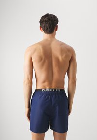 Pantaloni scurți de înot navy cu talie elastică și logo-ul Calvin Klein. Detaliu cu buzunar pe spate. Material neted, lungime deasupra genunchilor.