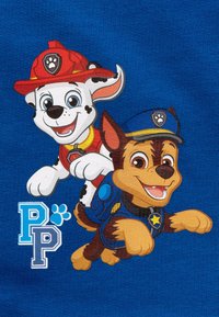 Graphic on blue fabric featuring two cartoon dogs: a white dog in a red firefighter hat and a brown dog in a blue police cap, with “PP” below.