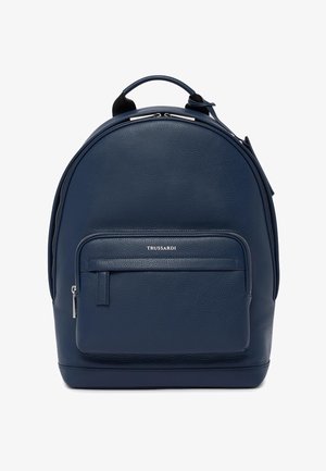 Mochila de cuero azul marino con forma redondeada, superficie texturizada, bolsillo frontal con cremallera y herrajes en tono plateado. Cuenta con correas ajustables y un asa superior.