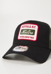 Gorra de béisbol negra con parte trasera de malla, que presenta un parche bordado en rojo y blanco que dice "BUFFALO, N.Y. New Era EST. 1920." Ajustable.