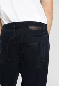 Mörka denimjeans med hög midja, med en slät textur, två bakfickor och en läderlogotyp på midjebandet.