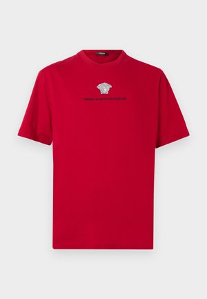 Červené bavlnené tričko s okrúhlym výstrihom. Dizajn obsahuje strieborné logo Medusa a text pod ním. Krátke rukávy a rovný spodný lem.