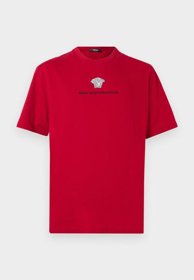 Κόκκινη βαμβακερή μπλούζα με στρογγυλή λαιμόκοψη. Διαθέτει ασημί λογότυπο Medusa και κείμενο από κάτω. Κοντά μανίκια και ίσια γραμμή στο κάτω μέρος.