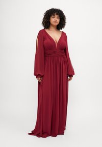 Long burgundy dress with a V-neck, pleated bodice, and flowing sleeves. Features open shoulders and a cinched waist for a loose fit.