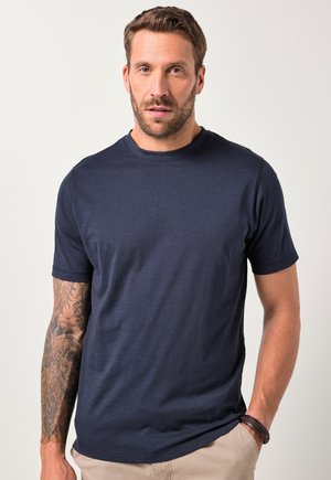 Navyblaue Kurzarm-T-Shirt aus einem weichen Material, mit Rundhalsausschnitt und glatter Textur. Das Modell mit sichtbarem Tattoo am Arm steht entspannt.
