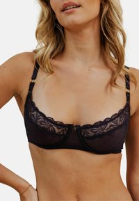 Soutien-gorge en dentelle noire avec un design en scallop, tissu transparent, soutien-gorge à armatures et bretelles ajustables avec des accents dorés.