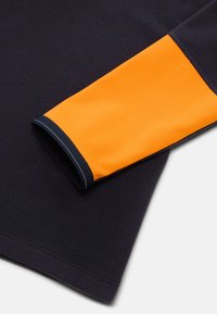 Marineblå fleecebeklædning med en orange elastisk manchet. Manchetten har en kontrastfarvet blå kant, der giver en klar kant og struktureret udseende.