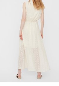 Maxikleid in Creme mit einem strukturierten, transparenten Überzug und einer taillierten Taille. Verfügt über ein ärmelloses Design und eine fließende Silhouette.