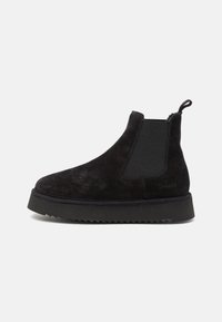 Botas Chelsea de ante negro con paneles laterales elásticos, lengüeta y suela de goma negra texturizada. Diseño elegante y minimalista.