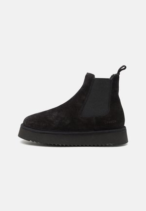 Botas Chelsea de camurça pretas com painéis laterais elásticos, uma aba para puxar e uma sola de borracha texturizada preta. Design elegante e minimalista.