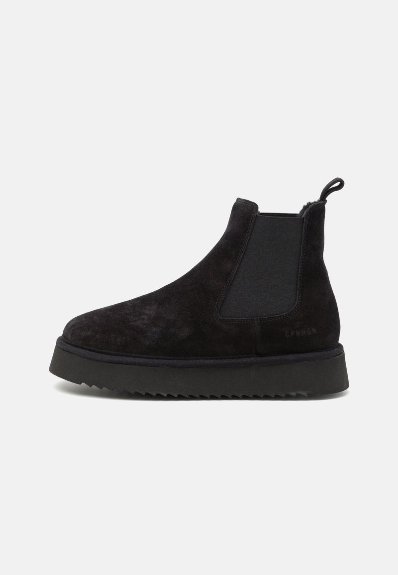 Bottines Chelsea en suede noir avec des panneaux élastiques sur les côtés, une bride de traction, et une semelle en caoutchouc noir texturé. Design élégant et minimaliste.