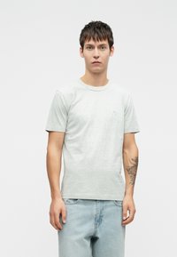 Light gray cotton t-shirt with short sleeves, crew neckline, and a small graphic detail on the chest, paired with light denim jeans.