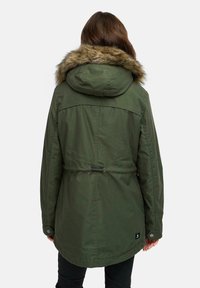 Olivengrön parka med fuskpäls på huvan, justerbart dragsnöre vid midjan och tryckknappar längs ärmarna.