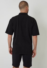 Schwarzes Polohemd mit kurzen Ärmeln aus strukturiertem Stoff, kombiniert mit passenden schwarzen Short. Minimalistisches Design und lockere Passform.