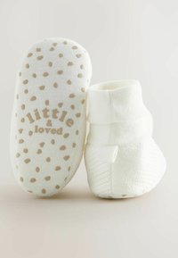 Chaussons en coton blanc avec une finition douce et texturée. Le dessous est orné de pois marron clair et du texte "petit & aimé" dans une couleur assortie.