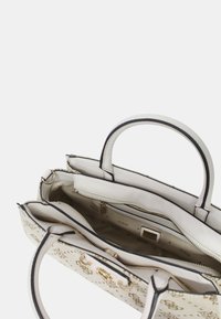 Sac à main blanc au design structuré, avec des accents noirs, deux poignées et une fermeture éclair. L'intérieur comporte plusieurs compartiments.