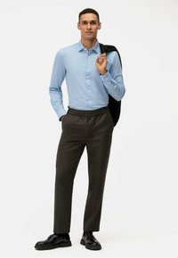 Camicia button-up blu chiaro, pantaloni con elastico in vita scuri, scarpe nere e un giubbotto nero appoggiato su una spalla; texture lisce.