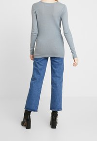 Grauer Strickpullover mit strukturiertem Muster, langen Ärmeln und rundem Ausschnitt, kombiniert mit blauen weiten Jeans und schwarzen Absatzstiefeln.