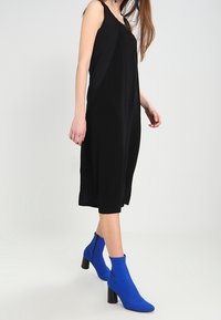 Czarna sukienka bez rękawów o luźnym kroju, zestawiona z niebieskimi botkami za kostkę z teksturowanym cholewką i słupkami.