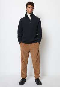 Navy knitted pullover with a half-zip collar, paired with light brown corduroy pants and black lace-up shoes. Simple, textured design.