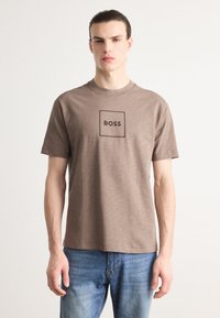 Brun bomulls t-skjorte med kort ermer og rund hals, med et kvadratisk logo med "BOSS" trykt i svart i sentrum.
