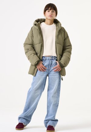 Doudoune vert olive avec capuche, fermeture éclair, poignets côtelés, associée à un pantalon en jean large bleu clair et des chaussures bordeaux.
