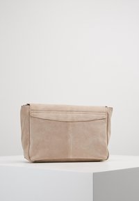 Beige semišová kabelka obdélníkového tvaru, hladkého povrchu a se skládací klopou. Obsahuje zipové uzavírání a jemné prošívání.