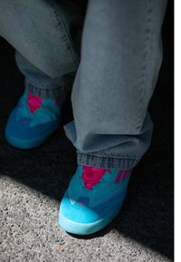 Lyse blå joggesko med rosa detaljer er delvis synlige, parret med lyse denimbukser, hviler på en teksturert grå overflate.