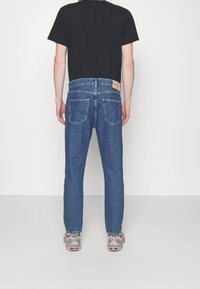 Blå denimjeans med rak passform, synlig sömnad, två bakfickor och en ljusbrun läderlapp fäst vid midjan.