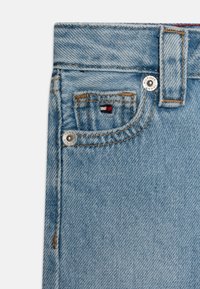 Light blue denim fabric with a front pocket, featuring contrasting stitching and a small logo tag. Includes metal hardware details.